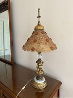 Full view of lamp on table showing cherub base, shade, cord