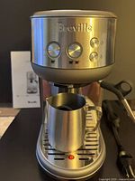 Front view of Breville Bambino BES450 espresso machine with control buttons and frothing pitcher on drip tray