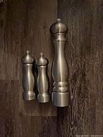 Three stainless Peugeot grinders aligned on floor, showing size difference