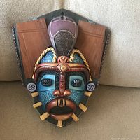 Front view of colorful tribal wall mask showing overall design and dimensions relative to couch