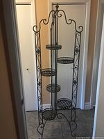 Full view of tall foldable wrought iron plant stand with six round shelves