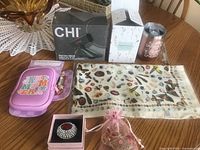 Overview of all six items: CHI stand box, two tumblers, pink pouch, printed scarf, brooch in box and brooch in organza bag