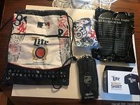 Group shot of all five promotional items: one knapsack out of packaging, second knapsack sealed, flip-flops package, gloves package, boxed T-shirt