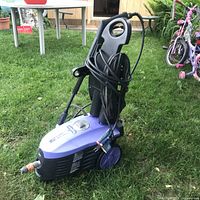 Full view of pressure washer showing housing, wheels, cord and hose wrapped, spray gun attached