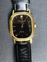 Front view showing gold-tone rectangular watch case, black dial, leather strap