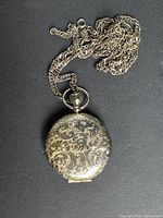 Front view of compact on chain showing ornate engraving