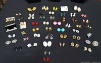 Full layout showing 49 pairs of clip-on earrings in rows on black cloth