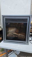 Front view of fireplace insert showing frame, glass, faux logs