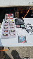 Overall lot on table: PS One, Genesis, SNES cartridges, PlayStation game stack, cables