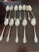 Twelve matching sterling teaspoons laid out bowl up showing overall design and wear