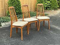Front angled view of all three teak chairs showing design and upholstery