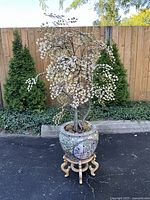 Full view of porcelain jardiniere on wooden stand with faux tree