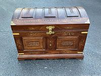 Front view showing domed lid, carved panels, brass latch and corner straps