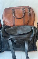 Front view of brown Fossil briefcase and black duffle