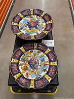 Two hand-painted floral plates on black bin
