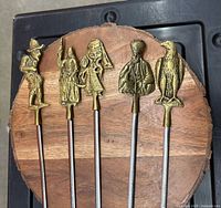 Five skewers with brass handles displayed in wood stand