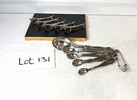 Full lot showing five dachshund rests and ring of measuring spoons