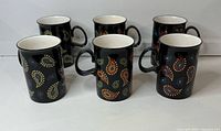 Front view of six black paisley mugs