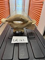 Front view of bone sculpture on black platform showing two whales and attached tag