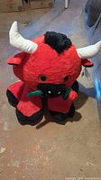 Full view of red plush bull showing horns, hooves and flower accessory