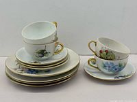 Stack of dessert plates and saucers with two teacups showing hand-painted designs