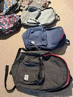 Four of the six backpacks laid out: floral Vans, light grey heather, navy Herschel, charcoal Herschel