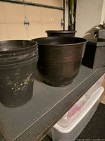 Group of plastic pots on shelf: nested nursery pots, large round planter, square planter