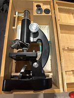 Microscope seated in wooden case with accessories visible