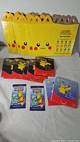 Stack of unassembled Pikachu Happy Meal boxes, eight toy envelopes and two sealed booster packs