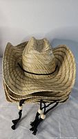 Stack of straw cowboy hats showing crown shape, chin cord, wooden beads