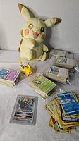 Overall lot showing Pikachu plush, plastic Pikachu figure, stacks of bagged cards, loose cards and sleeved card