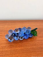 Side view of blue glass grape cluster with green leaf on wood surface
