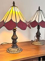 Front view of both matching stained glass lamps lit on wooden surface