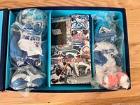 Open presentation box showing three sealed plush toys, guide booklet and lapel pin