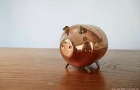 Front view of copper/brass piggy bank showing ears, snout and legs