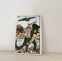 Front view of ceramic dinosaur light switch cover showing full painted design and screw holes