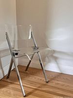 Full view of clear acrylic folding chair standing on hardwood floor