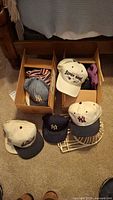 Boxes and floor display of multiple baseball hats including Yankees, Super Bowl and others
