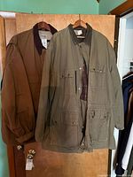 Two jackets on hangers: brown Carhartt FR and olive field jacket