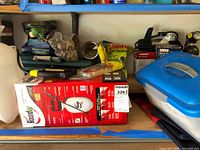 Shelf with boxed Roundup sprayer, bagged rocks, fertilizer, hydraulic jack box, air compressor, plastic bin with cords