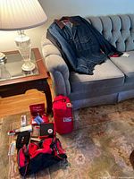 Overall lot showing jackets on sofa, duffel, sleeping bag, accessories on floor