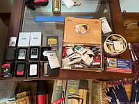 Overall lot view showing Zippo lighters in cases and boxes, matches in cigar box and tin, plus sealed Diamond match box