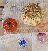 Four art glass pieces: gold mottled pumpkin, orange pumpkin, clear ornament with blue star, purple ribbed ornament