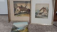 All three artworks: two framed cottage/chalet prints and one unframed lake landscape