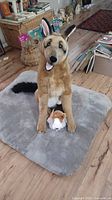 Large stuffed dog standing on grey dog bed with small plush puppy between its front legs