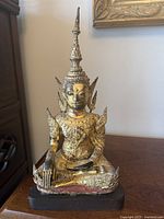 Front view of gilded seated Buddha on wood stand