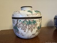 Front view of porcelain jar displaying hand-painted grapevine design and bronze rim