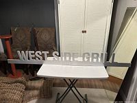 Front view of WEST SIDE GRILL silver-tone metal sign on folding table