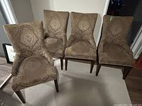 Front view of four upholstered dining chairs showing patterned fabric, seat shape and wooden legs