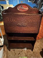 Front view of closed secretary showing carved panel, shelf and mirror
